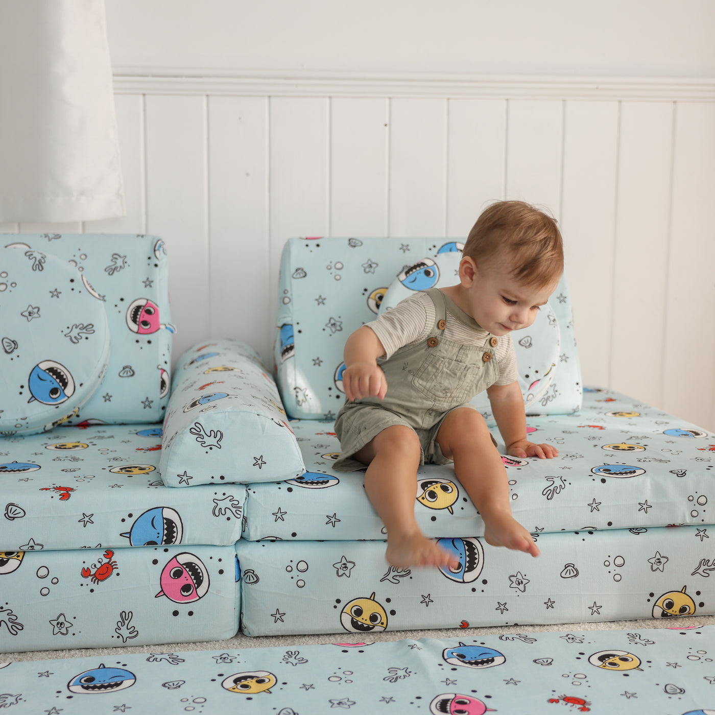 Toddler sitting on the Baby Shark™ x Roo & You™ Joey Play Couch in a bright playroom.